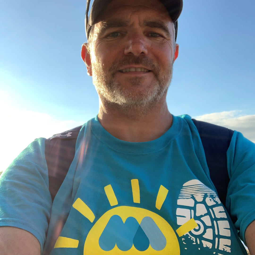 Man in cap with Miscarriage Association Miles That Matter t-shirt on, with blue sky behind him.