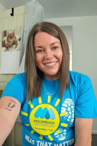 Josephine smiling and wearing a bright blue Miles That Matter t-shirt, sitting indoors with her arm resting on a table