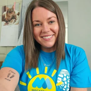 Josephine smiling and wearing a bright blue Miles That Matter t-shirt, sitting indoors with her arm resting on a table