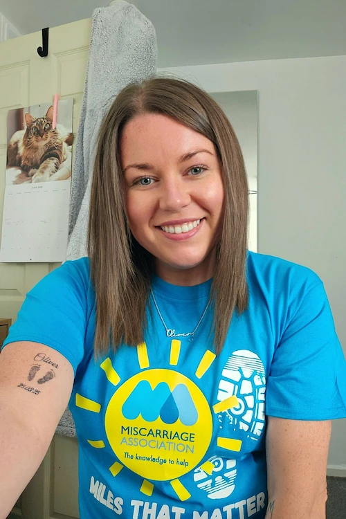 Josephine smiling and wearing a bright blue Miles That Matter t-shirt, sitting indoors with her arm resting on a table