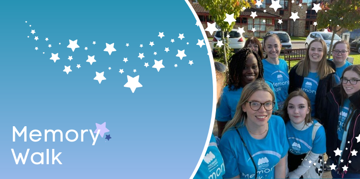 Group of Miscarriage Association supporters in blue Memory Walk t-shirts smiling together outdoors, with banner text 'Memory Walk' and star graphics