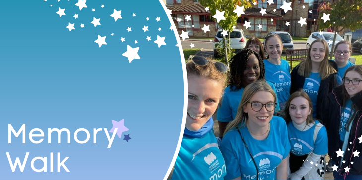 Group of Miscarriage Association supporters in blue Memory Walk t-shirts smiling together outdoors, with banner text 'Memory Walk' and star graphics.