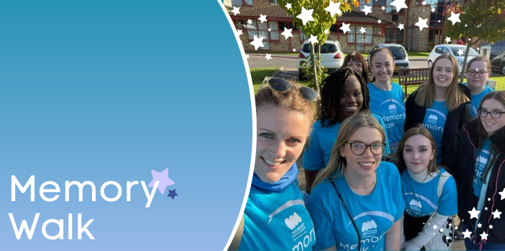 Group of Miscarriage Association supporters in blue Memory Walk t-shirts smiling together outdoors, with banner text 'Memory Walk' and star graphics