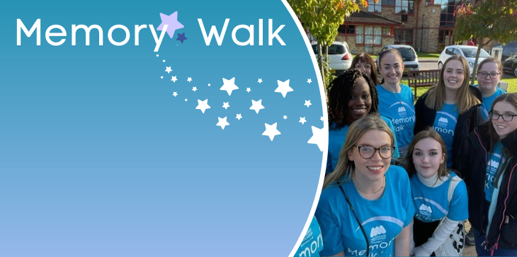 Group of Miscarriage Association supporters in blue Memory Walk t-shirts smiling together outdoors, with banner text 'Memory Walk' and star graphics